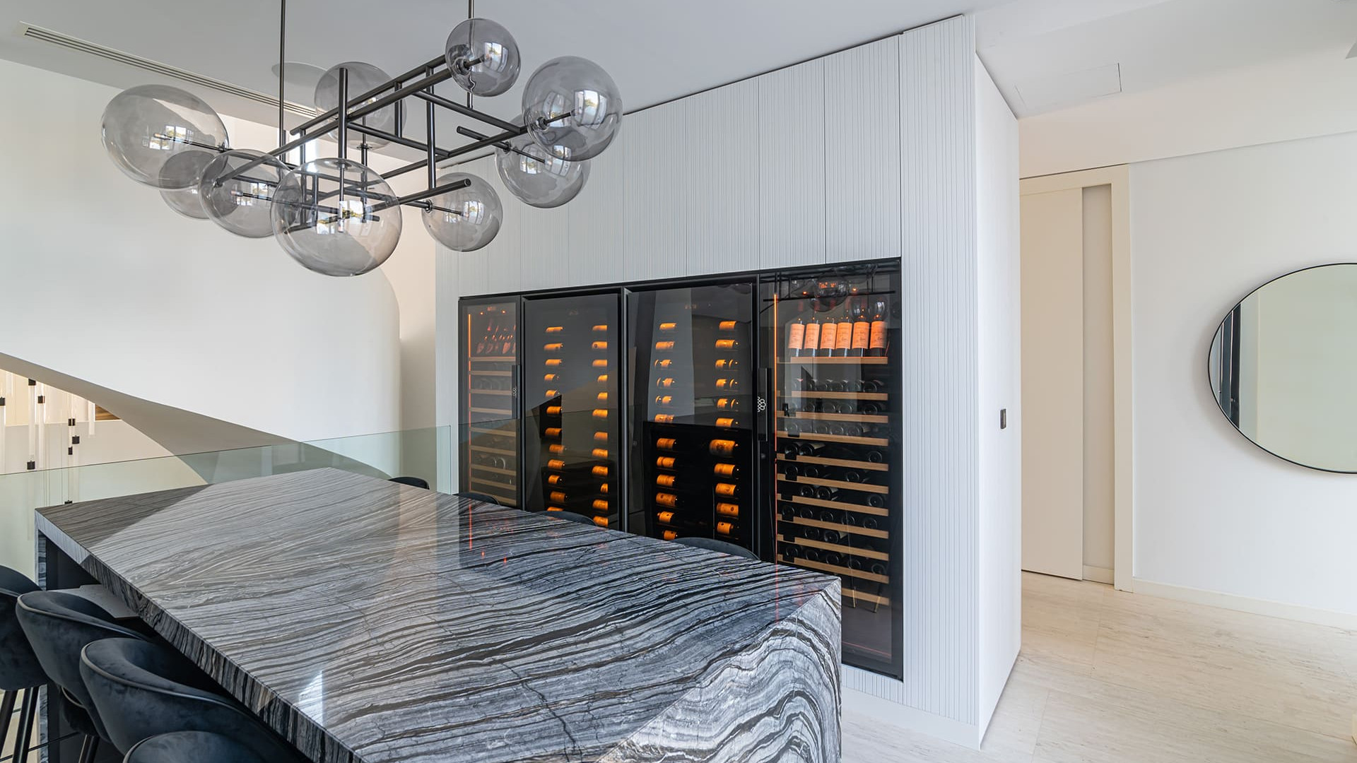 Vier in einen maßgeschneiderten Schrank eingebaute Weinkhülschränk in einem Wohngebäude mit prestigeträchtigem Innenarchitektur. Im Vordergrund ein langer Marmortisch. - Royale EuroCave Vier in einen maßgeschneiderten Schrank eingebaute Weinkhülschränk in einem Wohngebäude mit prestigeträchtigem Innenarchitektur. Im Vordergrund ein langer Marmortisch. - Royale EuroCave